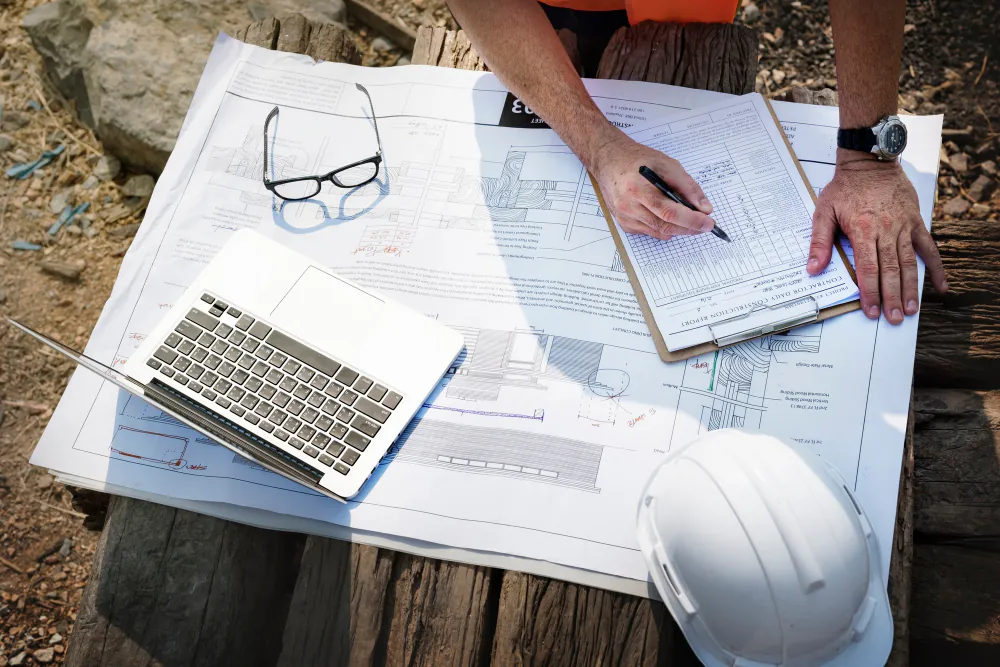 Estimator marking up plans with a laptop and hard hat